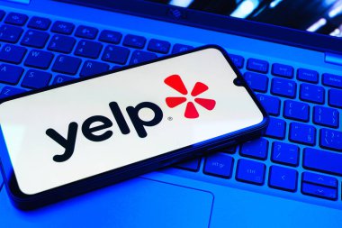 Prag, Çek Cumhuriyeti - 08 01 2025: Laptop klavyesinde duran bir cep telefonu Yelp logosunu gösterir. Yelp yerel işletmeleri bulmak ve incelemek için bir platformdur.