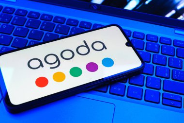 Prag, Çek Cumhuriyeti - 08 01 2025: Dizüstü bilgisayarın üzerinde duran bir cep telefonu Agoda logosunu gösteriyor. Agoda, otelleri ve seyahat yerlerini ayırtmak için bir platform..