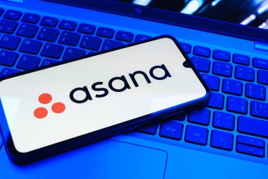 Prag, Çek Cumhuriyeti - 08 01 2025: Dizüstü bilgisayarın üzerinde duran bir cep telefonu Asana logosunu gösterir. Asana görev yönetimi ve takım işbirliği için bir platformdur..