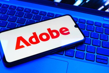 Prag, Çek Cumhuriyeti - 08 01 2025: Dizüstü bilgisayarın üzerinde duran bir cep telefonu Adobe logosunu gösterir. Adobe yaratıcı araçlar ve hizmetler sunan bir yazılım şirketidir..