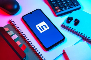 Prag, Çek Cumhuriyeti - 08 18 2025: Merkezde LinkedIn logosunu gösteren bir cep telefonu ile ofis malzemeleri düzenlemesi. LinkedIn, insanları ve şirketleri birbirine bağlayan profesyonel bir ağ..