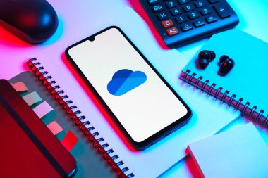Prag, Çek Cumhuriyeti - 08 18 2025: Merkezde OneDrive logosunu gösteren bir cep telefonu ile ofis malzemeleri düzenlemesi. OneDrive dosyaları kaydetmek ve paylaşmak için bir bulut depolama platformudur.