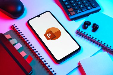 Prag, Çek Cumhuriyeti - 08 18 2025: Merkezde Powerpoint logosunu gösteren bir cep telefonu ile ofis malzemeleri düzenlemesi. Powerpoint sunumlar ve slayt gösterileri oluşturmak için bir yazılımdır..