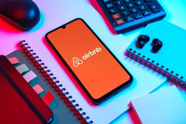 Prag, Çek Cumhuriyeti - 08 18 2025: Merkezde Airbnb logosu sergilenen bir cep telefonu ile ofis malzemeleri düzenlemesi. Airbnb dünya çapında kısa vadeli konaklama için bir platformdur..