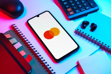 Prag, Çek Cumhuriyeti - 08 18 2025: Merkezde Mastercard logosu sergilenen bir cep telefonu ile ofis malzemeleri düzenlemesi. Mastercard ödeme kartları ve hizmetler sağlayan bir finans şirketidir..