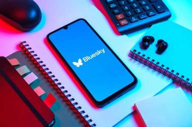 Prag, Çek Cumhuriyeti - 08 18 2025: Merkezde Bluesky logosunu gösteren bir cep telefonu ile ofis malzemeleri düzenlemesi. Bluesky merkezi olmayan ağlar için bir sosyal medya platformudur..