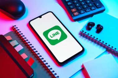 Prag, Çek Cumhuriyeti - 08 18 2025: Merkezinde hat logosu sergilenen bir cep telefonu ile ofis malzemeleri düzenlemesi. Line aramalar, mesajlar ve çokluortam paylaşımı için bir mesajlaşma uygulamasıdır.