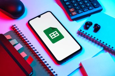 Prag, Çek Cumhuriyeti - 08 18 2025: Merkezde Google Sheets logosunu gösteren bir cep telefonu ile ofis malzemeleri düzenlemesi. Google Sayfalar tablo oluşturmak ve yönetmek için bir platformdur.