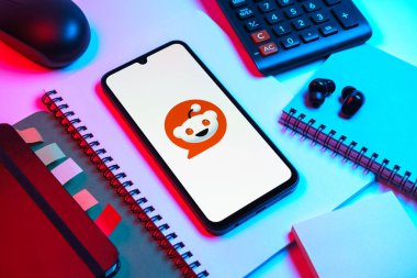 Prag, Çek Cumhuriyeti - 08 18 2025: Merkezde Reddit logosunu gösteren bir cep telefonu ile ofis malzemeleri düzenlemesi. Reddit tartışma, haber ve toplum içeriği için bir platformdur.