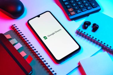 Prag, Çek Cumhuriyeti - 08 18 2025: Merkezde Google Sheets logosunu gösteren bir cep telefonu ile ofis malzemeleri düzenlemesi. Google Sayfalar tablo oluşturmak ve yönetmek için bir platformdur.