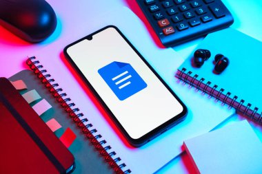 Prag, Çek Cumhuriyeti - 08 18 2025: Merkezde Google Docs logosunu gösteren bir cep telefonu ile ofis malzemeleri düzenlemesi. Google Docs metin belgeleri oluşturmak ve düzenlemek için bir platformdur.