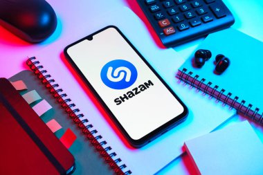 Prag, Çek Cumhuriyeti - 08 18 2025: Merkezinde Shazam logosu bulunan bir cep telefonu ile ofis malzemeleri düzenlemesi. Shazam şarkıları ve müzik parçalarını tanımlamak için bir uygulamadır.