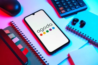 Prag, Çek Cumhuriyeti - 08 18 2025: Merkezde Agoda logosunu gösteren bir cep telefonu ile ofis malzemeleri düzenlemesi. Agoda, otelleri ve seyahat yerlerini ayırtmak için bir platform..