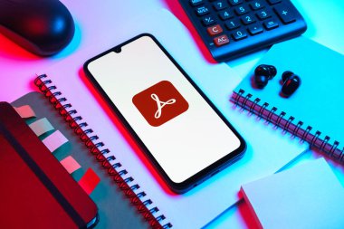 Prag, Çek Cumhuriyeti - 08 18 2025: Merkezinde Acrobat Reader logosu bulunan bir cep telefonu ile ofis malzemeleri düzenlemesi. Acrobat Reader, PDF belgelerini görüntülemek ve yönetmek için bir platformdur.