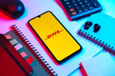 Prag, Çek Cumhuriyeti - 08 18 2025: Merkezde DHL logosu sergilenen bir cep telefonu ile ofis malzemeleri düzenlemesi. DHL uluslararası nakliye hizmeti sunan bir lojistik şirketidir..