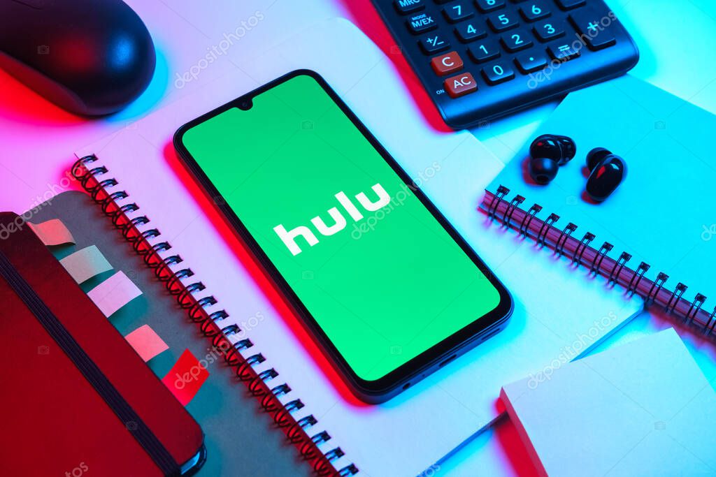 Prague, Czechia - 08 18 2025: An arrangement of office supplies with a mobile phone in the center displaying Hulu logo. Hulu is a streaming platform for TV shows, movies, and live TV.