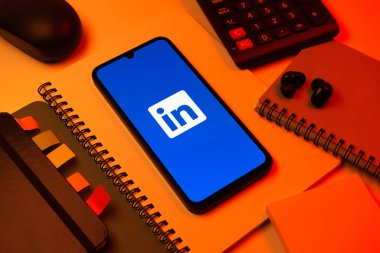 Prag, Çek Cumhuriyeti - 08 18 2025: Merkezde LinkedIn logosunu gösteren bir cep telefonu ile ofis malzemeleri düzenlemesi. LinkedIn, insanları ve şirketleri birbirine bağlayan profesyonel bir ağ..