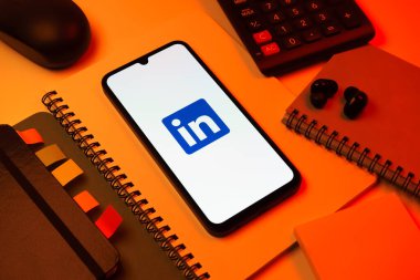 Prag, Çek Cumhuriyeti - 08 18 2025: Merkezde LinkedIn logosunu gösteren bir cep telefonu ile ofis malzemeleri düzenlemesi. LinkedIn, insanları ve şirketleri birbirine bağlayan profesyonel bir ağ..