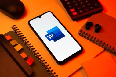 Prag, Çek Cumhuriyeti - 08 18 2025: Merkezinde Word logosu sergilenen bir cep telefonu ile ofis malzemeleri düzenlemesi. Word belge yaratmak ve düzenlemek için bir yazılımdır..