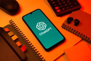 Prag, Çek Cumhuriyeti - 08 18 2025: Merkezinde ChatGPT logosu bulunan bir cep telefonu ile ofis malzemeleri düzenlemesi. ChatGPT metin üretmek ve soruları cevaplamak için bir yapay zeka sohbet robotudur..