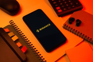 Prag, Çek Cumhuriyeti - 08 18 2025: Merkezde Binance logosunu gösteren bir cep telefonu ile ofis malzemeleri düzenlemesi. Binance dijital varlıkların ticareti için bir kripto para değiş tokuşu.