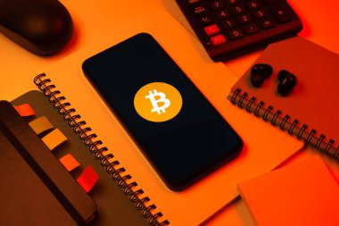 Prag, Çek Cumhuriyeti - 08 18 2025: Merkezde Bitcoin logosu sergilenen bir cep telefonu ile ofis malzemeleri düzenlemesi. Bitcoin merkezi olmayan işlemler için dijital bir kripto para birimidir.
