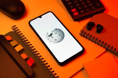 Prag, Çek Cumhuriyeti - 08 18 2025: Merkezinde Wikipedia logosu bulunan bir cep telefonu ile ofis malzemeleri düzenlemesi. Vikipedi çevrimiçi bir ansiklopedidir..