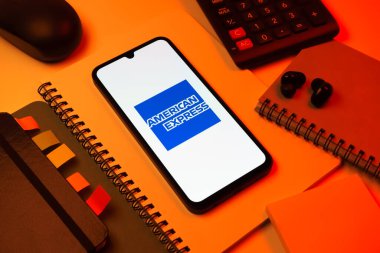 Prag, Çek Cumhuriyeti - 08 18 2025: Merkezde American Express logosunu gösteren bir cep telefonu ile ofis malzemeleri düzenlemesi. American Express kart ve bankacılık sunan bir finans şirketidir..