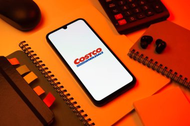 Prag, Çek Cumhuriyeti - 08 18 2025: Merkezde Costco logosunu gösteren bir cep telefonu ile ofis malzemeleri düzenlemesi. Costco toptan satış yapan bir perakendecidir. Üyelere toptan ürün satar..