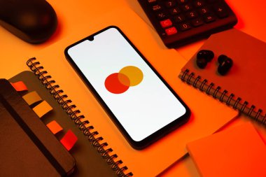 Prag, Çek Cumhuriyeti - 08 18 2025: Merkezde Mastercard logosu sergilenen bir cep telefonu ile ofis malzemeleri düzenlemesi. Mastercard ödeme kartları ve hizmetler sağlayan bir finans şirketidir..