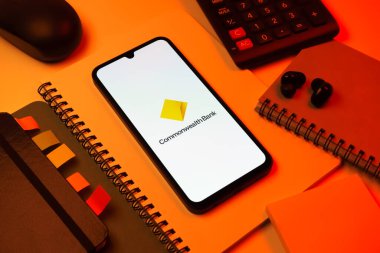 Prag, Çek Cumhuriyeti - 08 18 2025: Merkezinde Commonwealth Bank logosu bulunan bir cep telefonu ile ofis malzemeleri düzenlemesi. Commonwealth Bank, Avustralya 'da finansal hizmetler sağlayan bir bankadır..