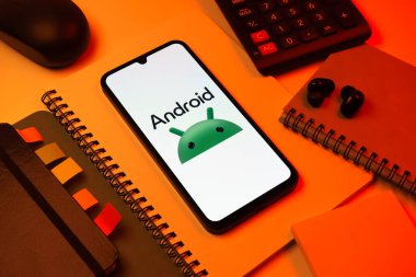 Prag, Çek Cumhuriyeti - 08 18 2025: Merkezde Android logosunu gösteren bir cep telefonu ile ofis malzemeleri düzenlemesi. Android akıllı telefonlar ve tabletler için mobil bir işletim sistemidir..