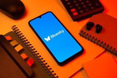 Prag, Çek Cumhuriyeti - 08 18 2025: Merkezde Bluesky logosunu gösteren bir cep telefonu ile ofis malzemeleri düzenlemesi. Bluesky merkezi olmayan ağlar için bir sosyal medya platformudur..