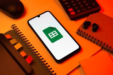 Prag, Çek Cumhuriyeti - 08 18 2025: Merkezde Google Sheets logosunu gösteren bir cep telefonu ile ofis malzemeleri düzenlemesi. Google Sayfalar tablo oluşturmak ve yönetmek için bir platformdur.