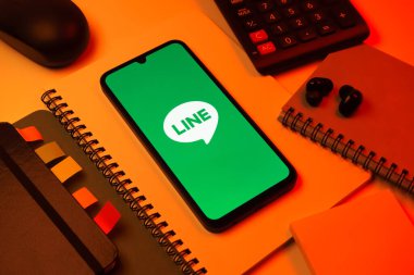 Prag, Çek Cumhuriyeti - 08 18 2025: Merkezinde hat logosu sergilenen bir cep telefonu ile ofis malzemeleri düzenlemesi. Line aramalar, mesajlar ve çokluortam paylaşımı için bir mesajlaşma uygulamasıdır.