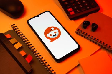 Prag, Çek Cumhuriyeti - 08 18 2025: Merkezde Reddit logosunu gösteren bir cep telefonu ile ofis malzemeleri düzenlemesi. Reddit tartışma, haber ve toplum içeriği için bir platformdur.