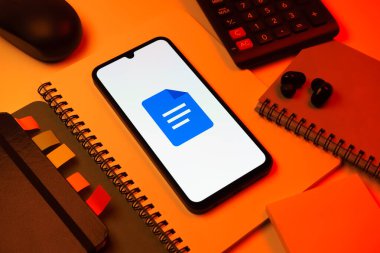 Prag, Çek Cumhuriyeti - 08 18 2025: Merkezde Google Docs logosunu gösteren bir cep telefonu ile ofis malzemeleri düzenlemesi. Google Docs metin belgeleri oluşturmak ve düzenlemek için bir platformdur.