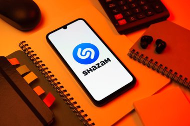 Prag, Çek Cumhuriyeti - 08 18 2025: Merkezinde Shazam logosu bulunan bir cep telefonu ile ofis malzemeleri düzenlemesi. Shazam şarkıları ve müzik parçalarını tanımlamak için bir uygulamadır.