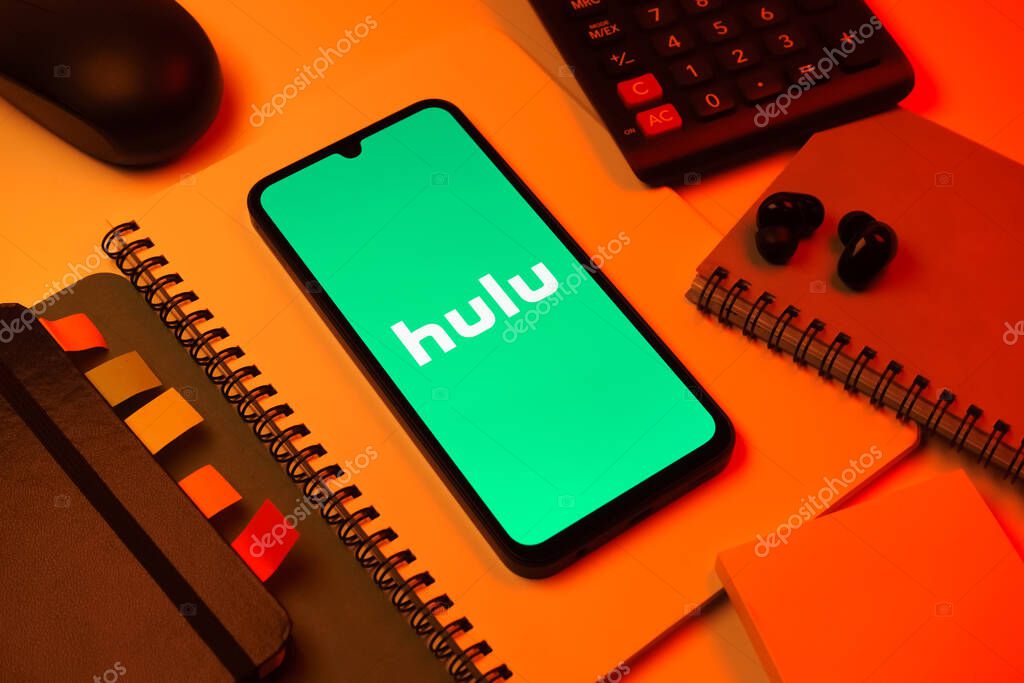 Prague, Czechia - 08 18 2025: An arrangement of office supplies with a mobile phone in the center displaying Hulu logo. Hulu is a streaming platform for TV shows, movies, and live TV.