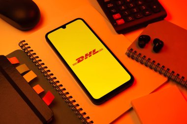 Prag, Çek Cumhuriyeti - 08 18 2025: Merkezde DHL logosu sergilenen bir cep telefonu ile ofis malzemeleri düzenlemesi. DHL uluslararası nakliye hizmeti sunan bir lojistik şirketidir..