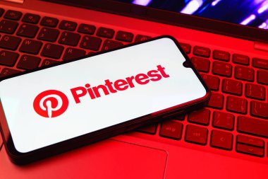 Prag, Çek Cumhuriyeti - 08 01 2025: Dizüstü bilgisayarın üzerinde duran bir cep telefonu Pinterest logosunu gösteriyor. Pinterest fikirleri görsel olarak keşfetmek ve kaydetmek için bir platformdur..