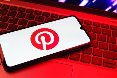 Prag, Çek Cumhuriyeti - 08 01 2025: Dizüstü bilgisayarın üzerinde duran bir cep telefonu Pinterest logosunu gösteriyor. Pinterest fikirleri görsel olarak keşfetmek ve kaydetmek için bir platformdur..