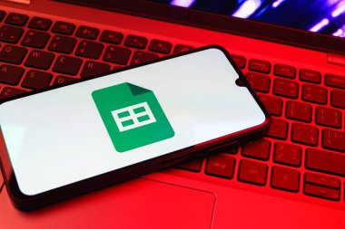Prag, Çek Cumhuriyeti - 08 01 2025: Laptop klavyesinde duran bir cep telefonu Google Sheets logosunu görüntüler. Google Sayfalar tablo oluşturmak ve yönetmek için bir platformdur.