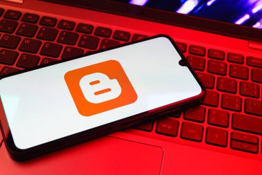 Prag, Çek Cumhuriyeti - 08 01 2025: Dizüstü bilgisayarın üzerinde duran bir cep telefonu Blogger logosunu gösterir. Blogger blog oluşturma ve yayınlama için bir platformdur.