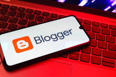 Prag, Çek Cumhuriyeti - 08 01 2025: Dizüstü bilgisayarın üzerinde duran bir cep telefonu Blogger logosunu gösterir. Blogger blog oluşturma ve yayınlama için bir platformdur.