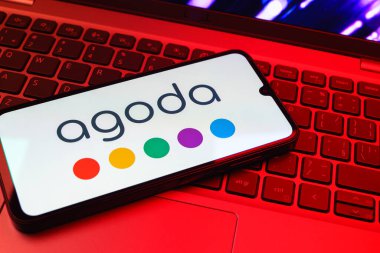 Prag, Çek Cumhuriyeti - 08 01 2025: Dizüstü bilgisayarın üzerinde duran bir cep telefonu Agoda logosunu gösteriyor. Agoda, otelleri ve seyahat yerlerini ayırtmak için bir platform..