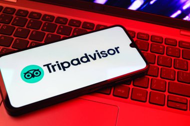 Prag, Çek Cumhuriyeti - 08 01 2025: Dizüstü bilgisayarın üzerinde bulunan bir cep telefonu TripDanışman logosunu gösteriyor. Seyahat danışmanı seyahat değerlendirmeleri, rezervasyonlar ve tavsiyeler için bir platformdur..