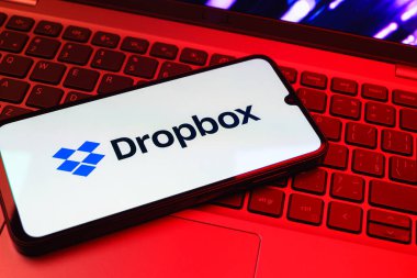 Prag, Çek Cumhuriyeti - 08 01 2025: Laptop klavyesinde duran bir cep telefonu Dropbox logosunu gösterir. Dropbox bulut depolama ve dosya paylaşımı için bir platformdur.