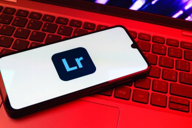 Prag, Çek Cumhuriyeti - 08 01 2025: Dizüstü bilgisayarın üzerinde duran bir cep telefonu Lightroom logosunu gösteriyor. Lightroom fotoğraf düzenleme ve yönetim için bir yazılımdır..
