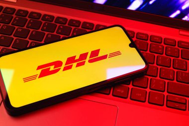 Prag, Çek Cumhuriyeti - 08 01 2025: Dizüstü bilgisayarın üzerinde duran bir cep telefonu DHL logosunu gösterir. DHL uluslararası nakliye hizmeti sunan bir lojistik şirketidir..